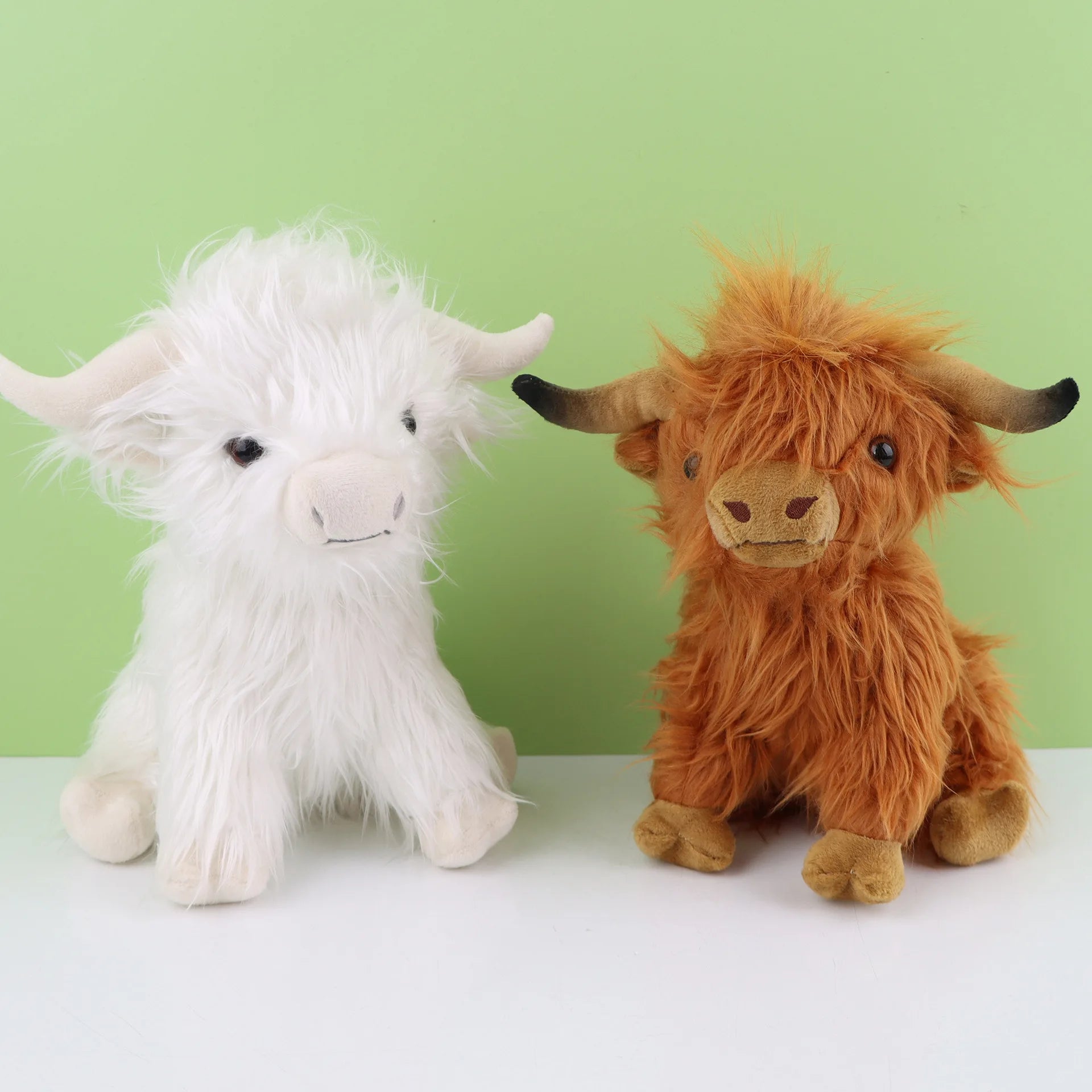 Two plush Highland cows, one white and one brown, on a light green background.